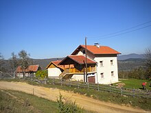 A white house with orange roof in a green field and blue sky