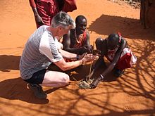 Cultural tourism in Kenya in 2005 Maasai people and a tourist lighting a fire in a Maasai village on the A109 road, Kenya.jpg