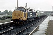 A Class 37 in British Rail large logo livery at Muir of Ord railway station, 1988 with a medium Route availability of 5. Muir of Ord railway station in 1988.jpg