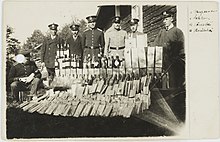 Illegal alcohol in confiscation, Finnish policemen and preventive officers on background. Prohibitory law against trade of alcoholic beverages ("kieltolaki") was in force during years 1919-1932 in Finland. Salakuljettajilta kieltolain aikana takavarikoitua alkoholia.jpg