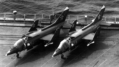 Två Jak-38 uppställda på däck. Båda är beväpnade med R-60 jaktrobotar. Vingarna är uppfällda och luckorna ovanför lyftmotorerna är öppna.