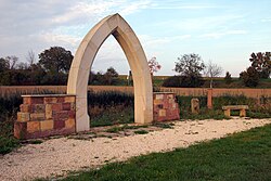 Arco gótico de piedra arenisca como monumento en la antigua ubicación, en el fondo la vegetación del río Hainbach