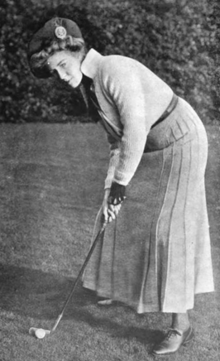 A white woman golfer wearing a hat, long sleeve top, and long pleated skirt, in a putting pose