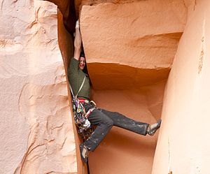 A woman is rock climbing. She hangs in a difficult spot.