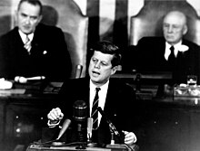 Președintele John F. Kennedy se adresează unei sesiuni comune a Congresului, cu vicepreședintele Lyndon B. Johnson și președintele Casei Sam Rayburn așezat în spatele lui