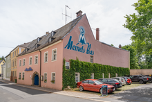 Das Foto zeigt das gebäude der Meinels Bas, ein Gebäude mit pinker Fassade und Logo