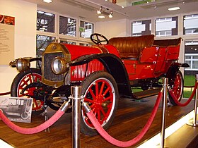 На фотографии показан автомобиль с откидным верхом 1913 года ярко-красного цвета.