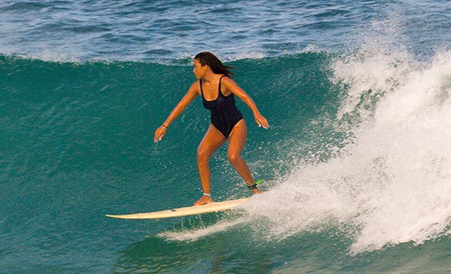 A girl surfing in a one-piece swimsuit