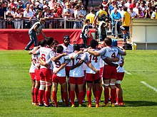 I giocatori di rugby vestiti con le loro maglie da gara si riuniscono in cerchio, tenendosi per le spalle.