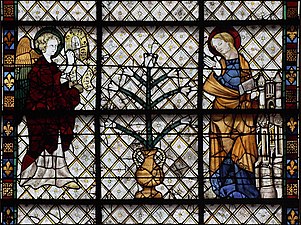 Glasmalerei.  Der Engel und Maria stehen zu beiden Seiten einer Vase mit einer großen Lilie.