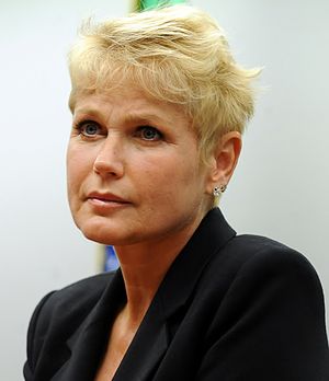 A blue-eyed blond woman with a pixie cut and stud earrings facing to her right.