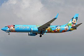 Sisi kiri dari sebuah pesawat berwarna dasar biru muda, disertai gambar Miki Tikus dan karakter Disney lainnya.