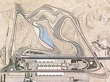 A tarmac motor circuit in a desert location, which is lined with concrete run-off areas, and features a large grandstand opposite the pit garages.