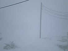 Blowing snow reduces visibility to several feet. The outline of a utility pole is barely visible in the background.