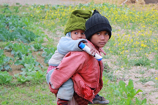 A Nepali child carries another child, "piggyback"