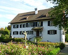 La maison abritant l'Institut C.G. Jung à Küsnacht. Il s'agit d'une petite maison vue de face, le toit recouvert de neige et tout autour de laquelle se trouvent des bosquets de conifères. La façade est légèrement de couleur rosée.