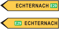 Richtung fir op Iechternach; dat iewescht Schëld steet op der Europastrooss E29; dat ënnescht Schëld weist un, datt een eréischt méi spéit op d'Europastrooss E29 kënnt.