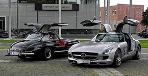 Two cars with open gullwing doors: an older black one and a gray one