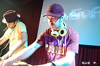 N.A.S.A. (DJ Zegon & Squeak E. Clean). The DJ on the left can be seen cuing up a part of a record by listening to the cue channel on one of his headphones. N.A.S.A. (DJ Zegon & Squeak E. Clean).jpg