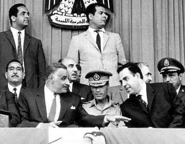 Gaddafi at an Arab summit in Libya in 1969, shortly after the September Revolution that toppled King Idris I. Gaddafi sits in military uniform in the middle, surrounded by Egyptian President Gamal Abdel Nasser (left) and Syrian President Nureddin al-Atassi (right).