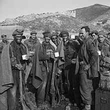 group of commandos with blackened faces drinking from cups. They have blankets around their shoulders and in the background are mountains