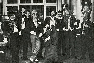 Photographie en noir et blanc d'un plateau de tournage cinématographique avec neuf personnages masculins et un ours vivant.