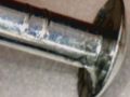 Closeup of stock Pinewood Derby car axle showing stamp marks (left) and nail head burr (lower right).