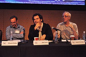 Three white men sat behind a table holding microphones and place cards