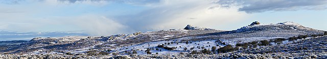 Dartmoor in winter covered in snow. Several tors top the sparsely vegetated hills.