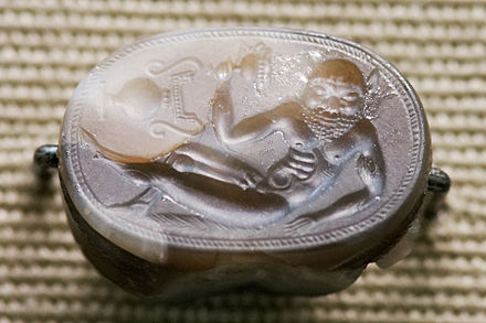 Reclining satyr, Etruscan c. 550 BC, 2.2 cm wide. Note the vase shown "sideways"; it is characteristic of early gems that not all elements in the design are read from the same direction of view.