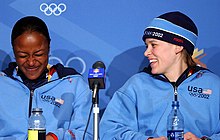 Photographie de deux femmes souriantes en conférence de presse, portant des survêtements bleu ciel.