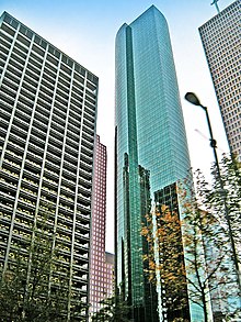 Tall, thin, glass tower with large, rounded outset on one side and strong vertical lines.