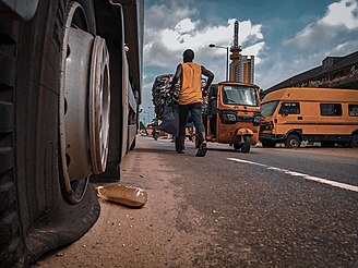 A flat tire in a busy district in Lagos, Nigeria. A vehicle with a flat tire can cause local delays in traffic. A broken down truck, A cart pusher, A tricycle and a bus in Lagos.jpg