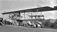 Curtiss NC-4 flying boat after it completed the first crossing of the Atlantic in 1919, standing next to a fixed-wing heavier-than-air aircraft Aircraft with people and buildings.jpg