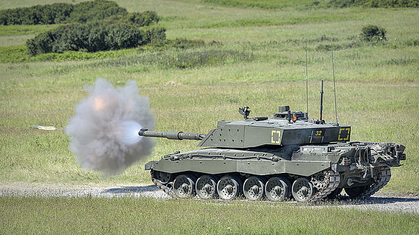 A Challenger 2 firing its main armament during an exercise. The shell is visible to the left of the smoke cloud.