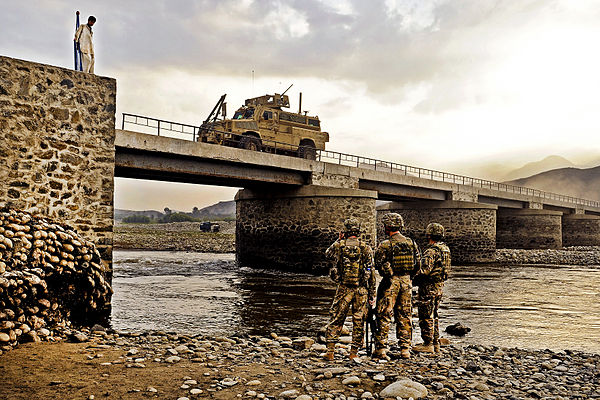 Members of the U.S. Air Force inspecting the underside of a bridge as traffic squeezes through the narrow roadway in Mihtarlam.