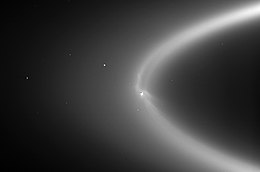 The backlit E ring, with Enceladus silhouetted against it at center. The moon's south polar jets erupt brightly below it, while tendrils of the E Ring wrap around it.