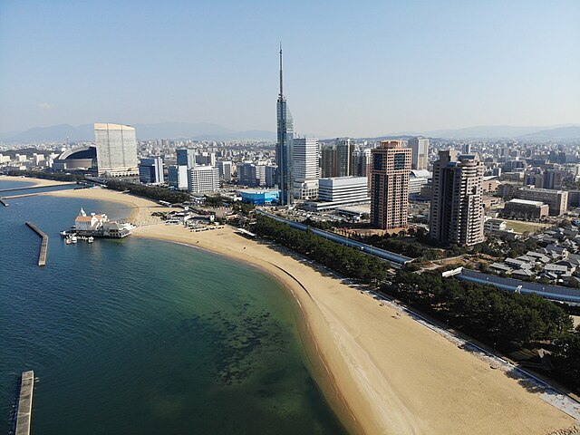 Aerial view of the seaside Momochi [ja] with the Fukuoka Tower and Momochi Seaside Park in the center and with the Fukuoka PayPay Dome to the left sid