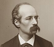 Portrait photographique en noir et blanc d'un homme portant lunettes et moustache noire.