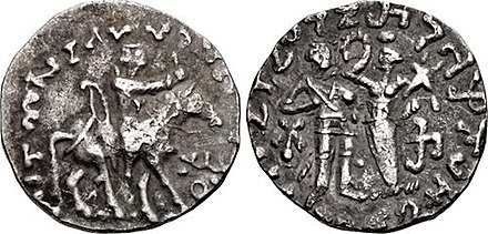 Coin of Zeionises (c. 10 BCE – 10 CE).Obv: King on horseback holding whip, with bow behind. Corrupted Greek legend MANNOLOU UIOU SATRAPY ZEIONISOU "Satrap Zeionises, son of Manigula". Buddhist Triratna symbol.Rev: King on the left, receiving a crown from a city goddess holding a cornucopia. Kharoshthi legend MANIGULASA CHATRAPASA PUTRASA CHATRAPASA JIHUNIASA "Satrap Zeionises, son of Satrap Manigul". South Chach mint.