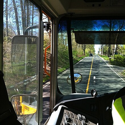 View behind school bus driver's compartment, showing multiple mirrors (rearview, convex, and crossview) and sun visor