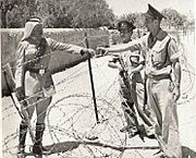 マンデルバウム門で撮影されたアラブ軍団（英語版）のヨルダン兵（左）とイスラエルの警察官（右）。イスラエルの警察官らはトミーガンで武装している（1950年頃）