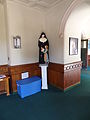 A statue of a nun and a child, and a food donation container, in the narthex of Saint Patrick Church. The nun's text is in French. The food donation container has text in both English and Spanish.