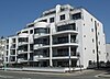 A five-storey white-painted building with a streamlined, curvaceous façade and large glass balconies