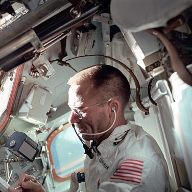 View from side of a white suited astronaught in an orbiting vessel writing with his right hand