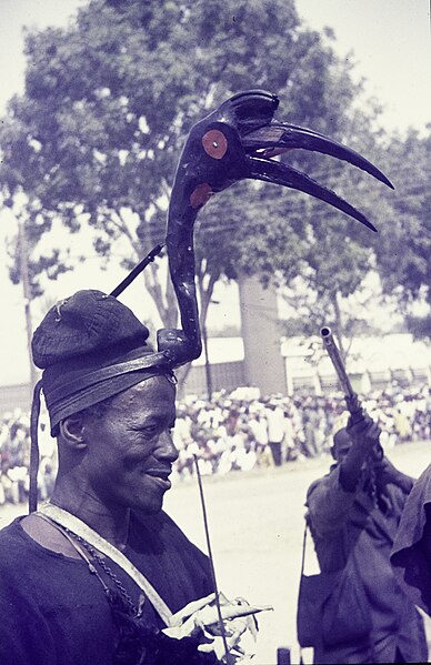 File:ASC Leiden - Rietveld Collection - Nigeria 1970 - 1973 - 01 - 065 Sallah festivities in Bauchi. A man outside with a hornbill diadem on his head. Another man aims at him with a gun. In the background a group in white.jpg