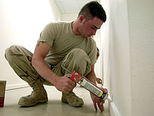 Man applying caulk to baseboard Caulking, USAF.jpg