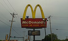 A blue Fry Kid is seen sitting on a McDonald's sign in Greenfield, Wisconsin. Fry Kid Perched on McDonald's Sign.jpg