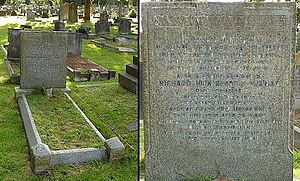 A granite headstone in the shade of a tree, surrounded by other gravestones