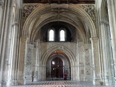 Au-dessus du portail, une pièce ouverte vers la nef et éclairée par deux fenêtres. Deux piliers sont visibles au premier plan. Sur ces derniers sont sculptés deux hauts reliefs représentant des femmes.